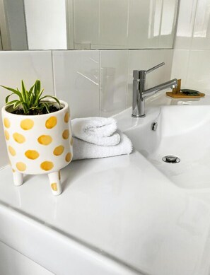 Een badkamer met een wit wastafel, een witte handdoek en een witte pot met stippen met een plant.