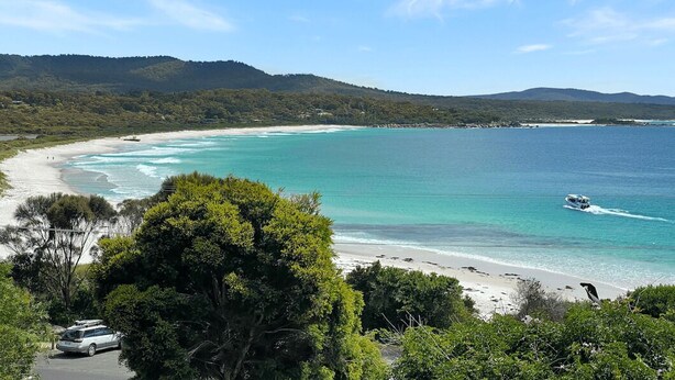 Eine Küstenlandschaft mit Strand, klarem türkisblauem Wasser und einem Fahrzeug in der Nähe des Ufers.