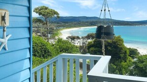 Eine Holzterrasse mit weißer Geländer, mit Blick auf Strand und Meer.