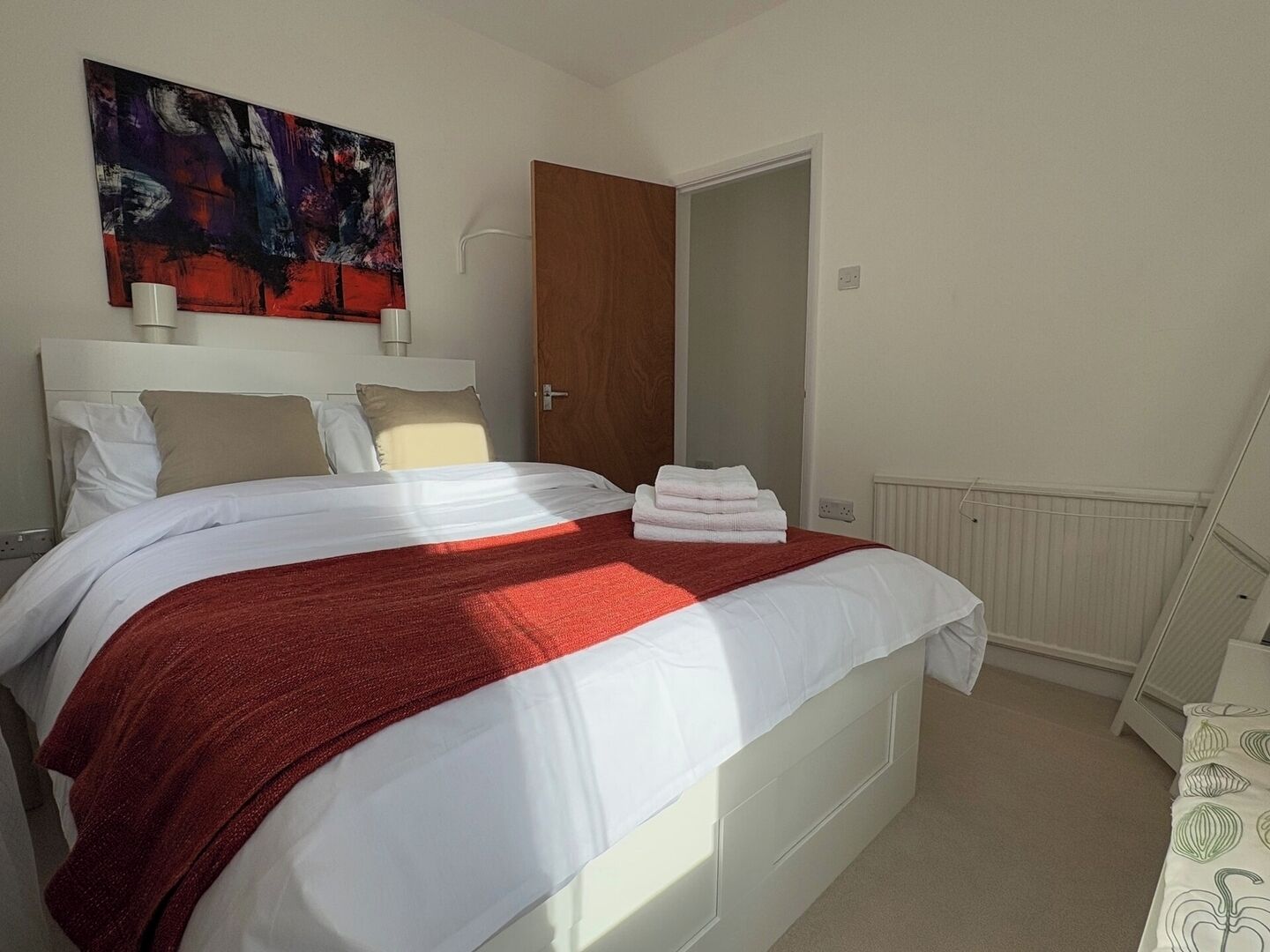 A bedroom with a bed, a door, a radiator, and a painting on the wall.