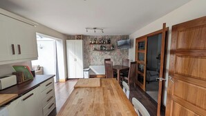 Eine Küche mit Holzausstattung, einem Essbereich mit Tisch und Stühlen, einer eingebauten Stellfläche für Flaschen und einem an der Wand montierten Fernseher.