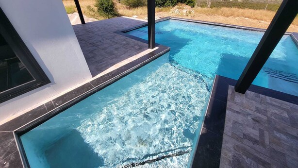 Een zwembad met helderblauw water, omringd door een modern gebouw met grote ramen.