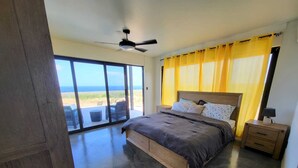 Een slaapkamer met een groot bed, een plafondventilator en uitzicht op de oceaan door grote ramen.