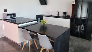 Een moderne keuken met een zwart aanrecht, twee grijze stoelen, een magnetron, een koffiezetapparaat en een koelkast.