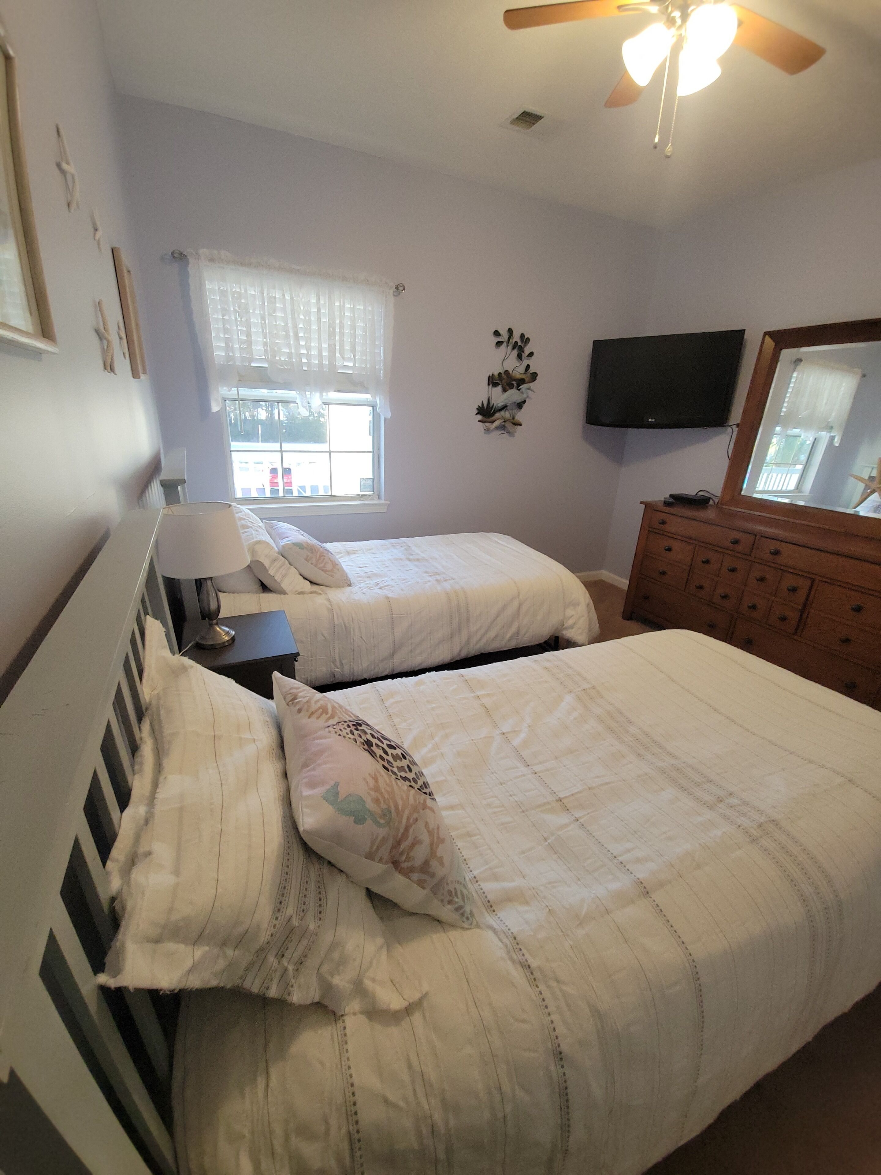 A bedroom with two beds, a dresser, a TV, and a ceiling fan.