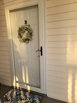 A white door with a wreath, a black doorbell, and a patterned doormat. - Paradise Found at Coastal Myrtle Beach 2B, 2B Condo (Myrtle Beach)