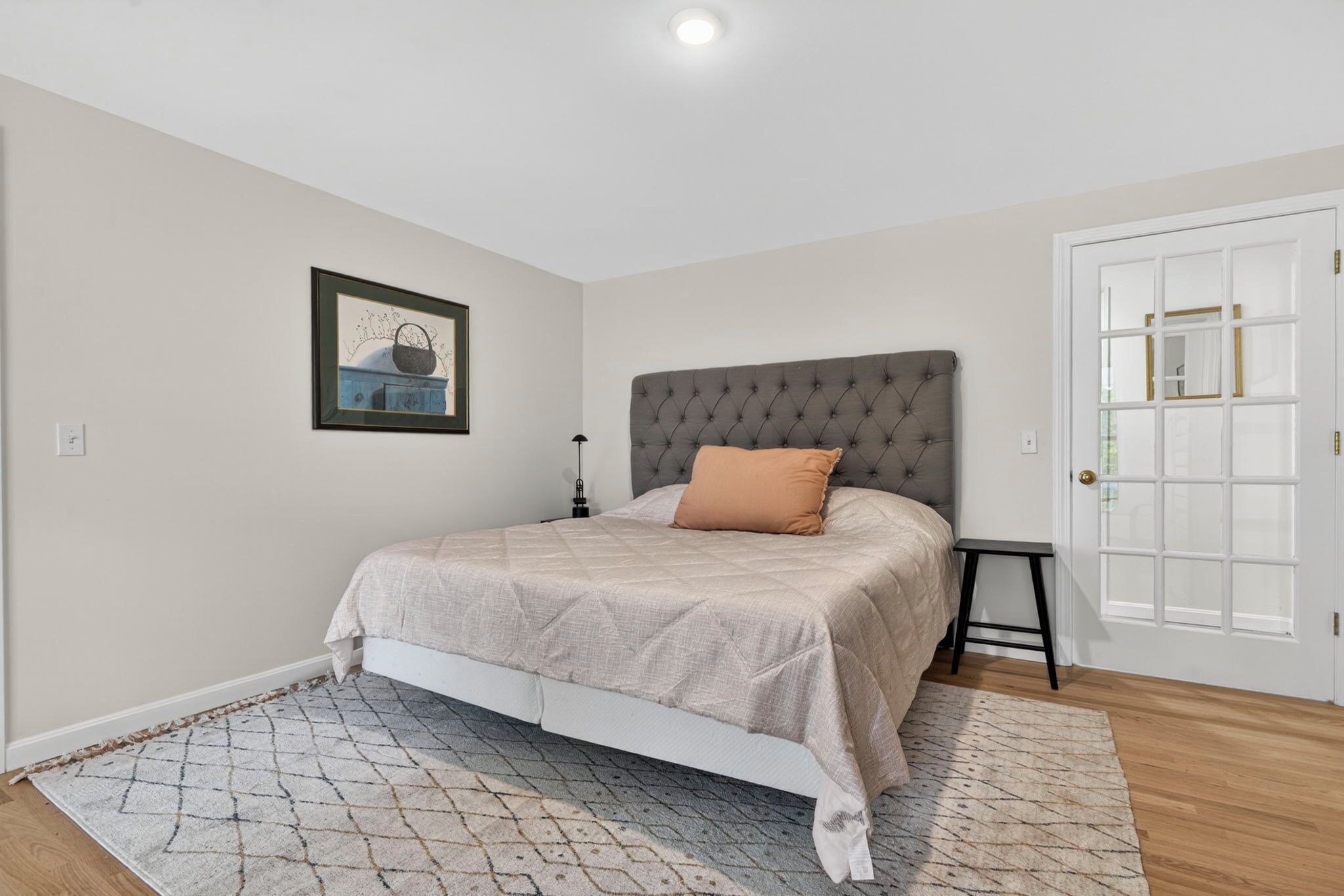 A bedroom with a bed, a nightstand, a framed picture, and a door with a window.