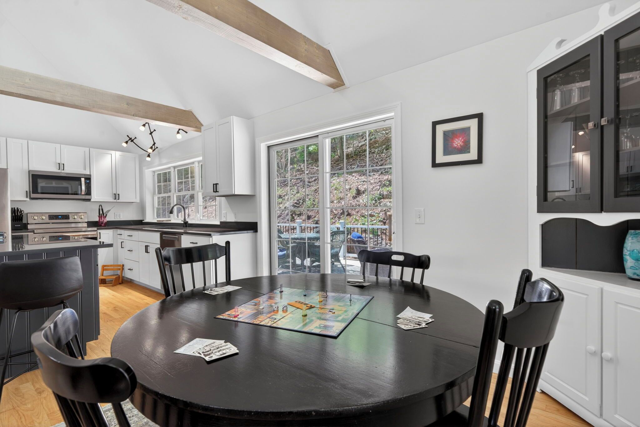 A modern kitchen with white cabinets, a dining table with chairs, and a view through large glass doors.