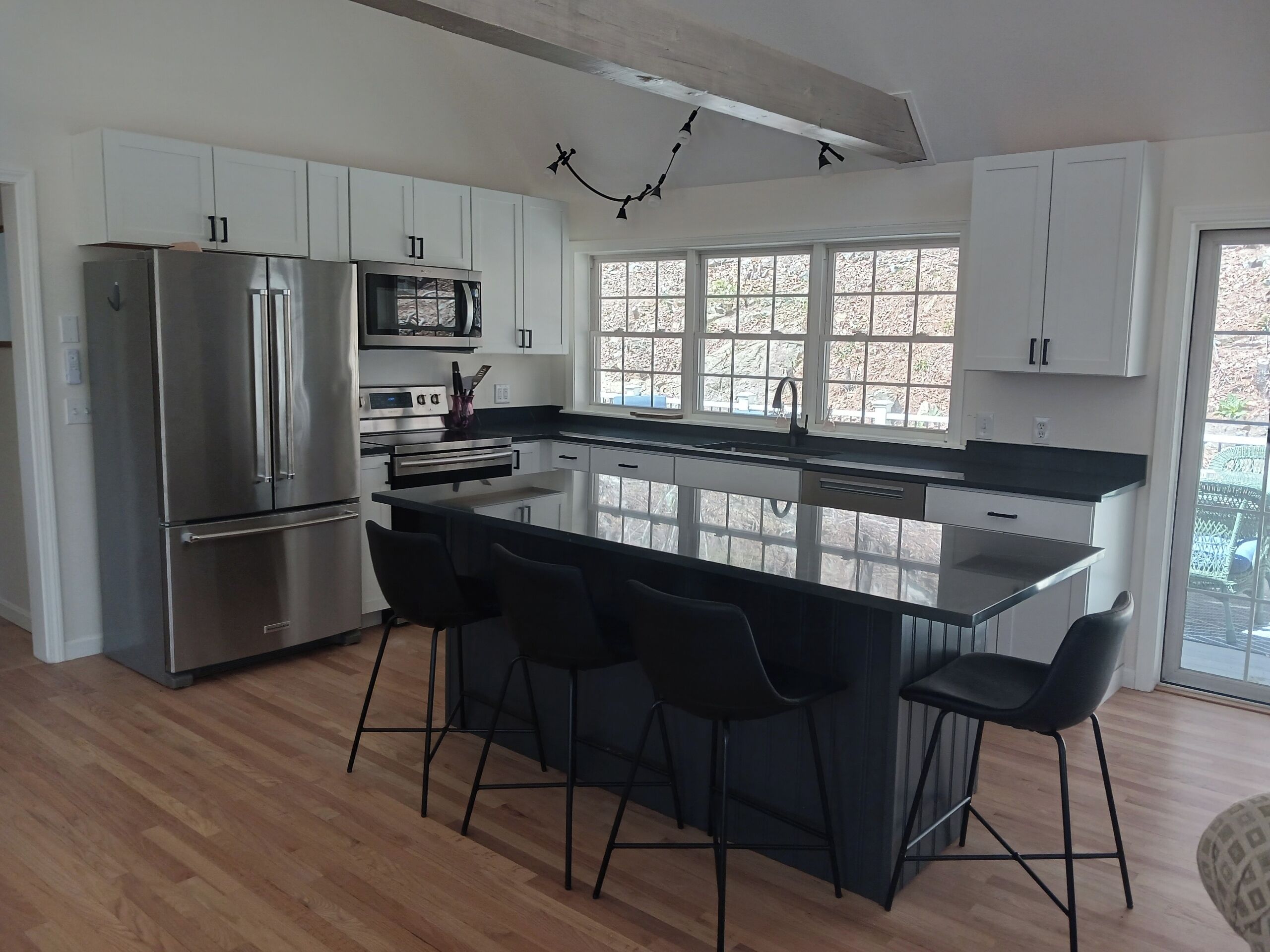 A modern kitchen with a central island, stainless steel appliances, and a large window.