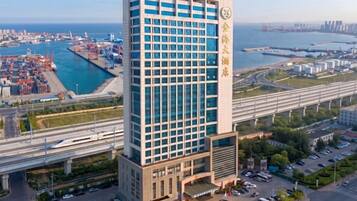 A high-rise hotel with a modern design, located near a body of water and a busy port area.