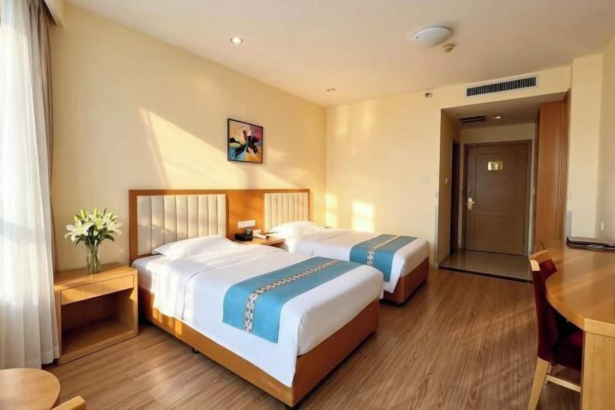 Hotellihuone, jossa on kaksi sänkyä, puulattia, työpöytä ja ovi.
