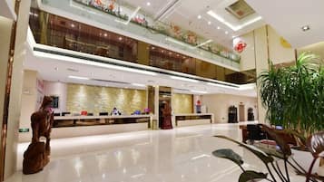 A spacious lobby with a reception desk, a staircase, and a large plant.