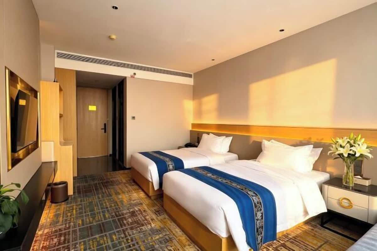 A hotel room with two beds, a TV, a desk, and a vase with flowers.
