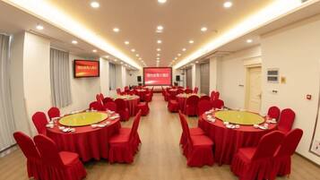 A conference room with multiple round tables, red chairs, and a large screen at the front.