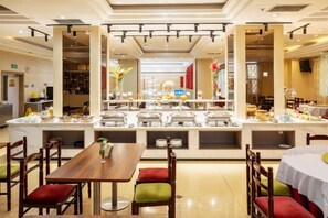 Un'area ristorazione in hotel con diversi tavoli e sedie, un angolo buffet e vista sul ristorante adiacente.
