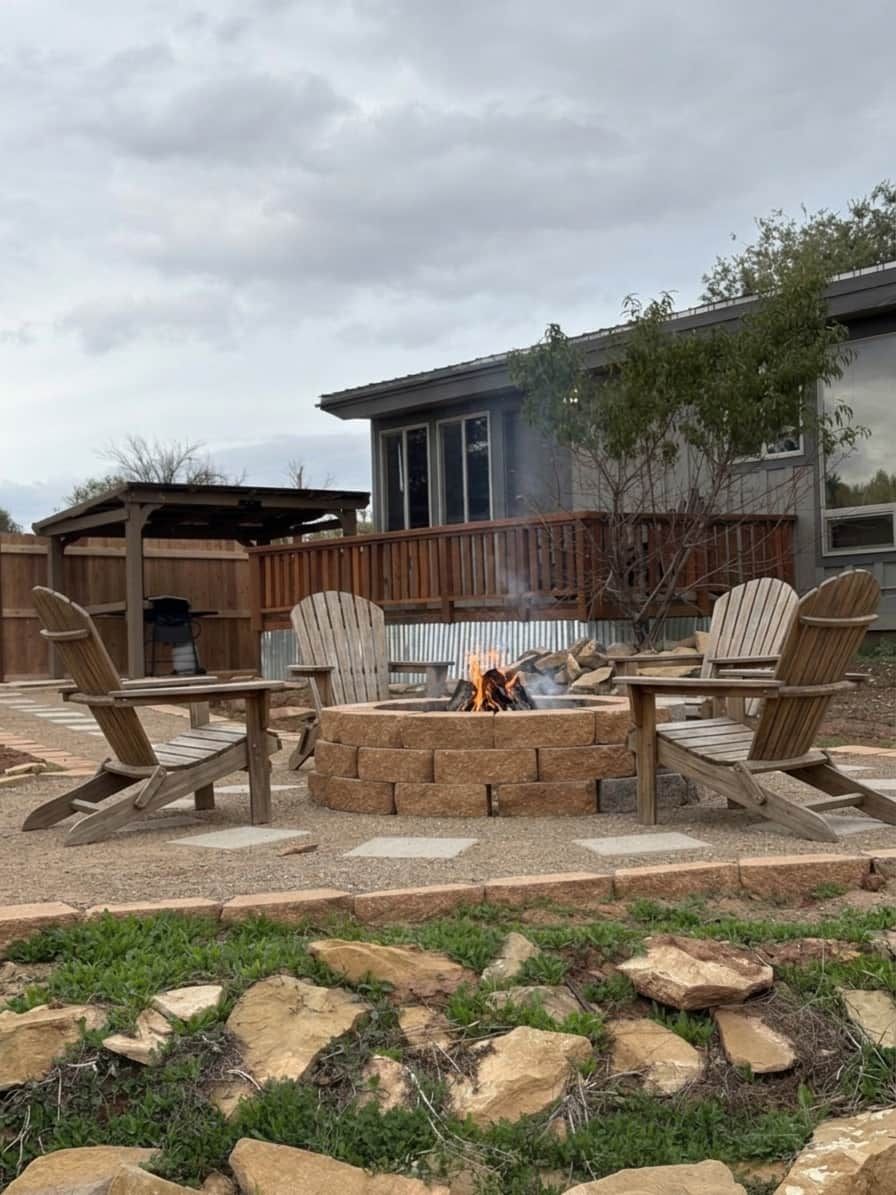 A backyard with a fire pit, wooden chairs, and a barbecue grill.