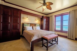 A bedroom with a bed, a bench, a ceiling fan, and a window with a view.