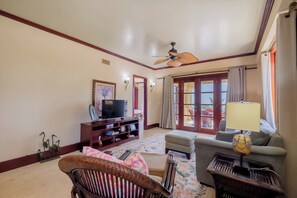 A living room with a television, a ceiling fan, a sofa, a patterned rug, and a window with curtains.