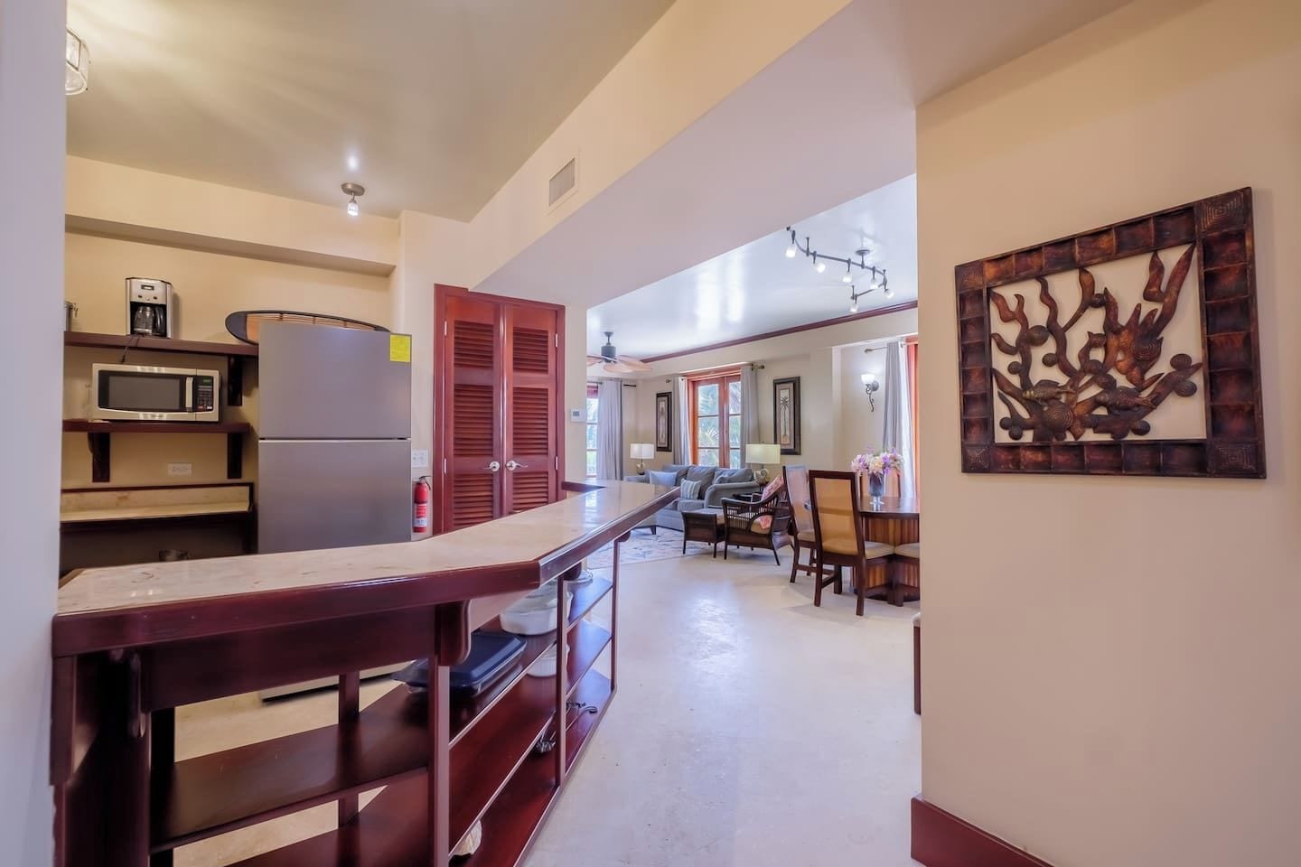 A kitchen with a microwave, refrigerator, and wooden cabinets. There is a dining area with a table and chairs.