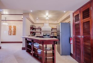 A modern kitchen with a central island, built-in shelves, and a stainless steel refrigerator.