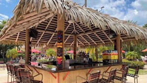 Eine Bar mit Strohdach, Holzhockern und einer Theke.