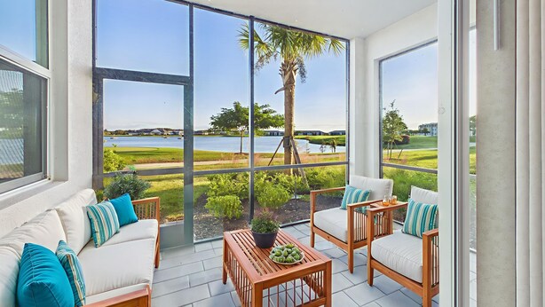 A spacious balcony with a white sofa, wooden chairs, and a table, overlooking a lake and greenery. - Enjoy a luxury 2BR/2BA Condo in beautiful Ave Maria Golf and Country Club (Ave Maria)