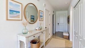 A hallway with a white console table, a mirror, framed pictures, and a door leading to another room. - Enjoy a luxury 2BR/2BA Condo in beautiful Ave Maria Golf and Country Club (Ave Maria)