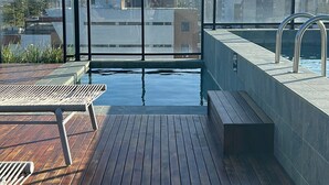A rooftop pool with wooden decking, a lounge chair, and a view of the city skyline. - Apartment / Beachfront / Pool / Intermares (Cabedelo)