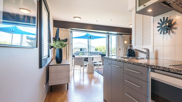 Una cocina moderna con un amplio ventanal, un comedor con mobiliario exterior y un reloj decorativo en la pared.