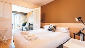 Una habitación de hotel con una cama grande, una mesita de noche con lámpara, un escritorio pequeño y una silla.