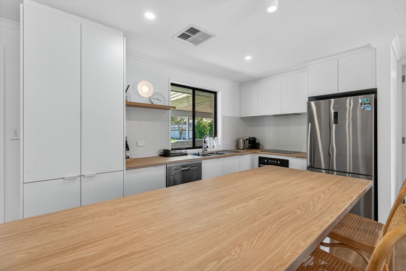 A modern kitchen with white cabinetry, a wooden countertop, a stainless steel refrigerator, and a window providing natural light.