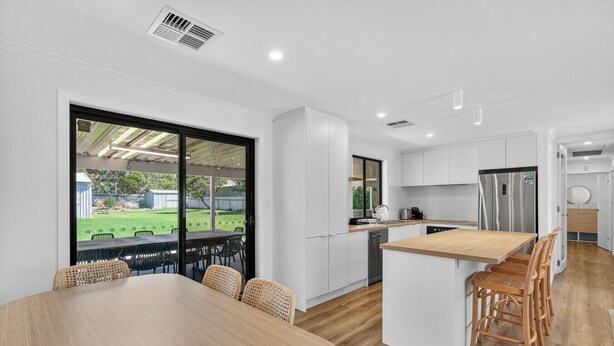 A modern kitchen with white cabinetry, a wooden island, and a dining area with wicker chairs. - Perfect Family Escape (Port Elliot)