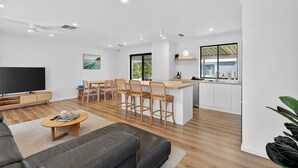 A modern living room with a flat-screen TV, a sofa, and a dining area with wooden chairs and a table. - Perfect Family Escape (Port Elliot)