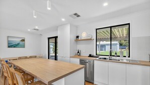 A modern kitchen with a wooden dining table, white cabinets, and a large window. - Perfect Family Escape (Port Elliot)