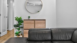 A modern living room with a grey leather sofa, a wooden cabinet with a plant, and a round mirror on the wall. - Perfect Family Escape (Port Elliot)