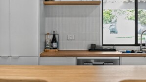 A modern kitchen with a wooden countertop, a built-in dishwasher, and a window with a view of greenery. - Perfect Family Escape (Port Elliot)