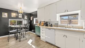 A modern kitchen with white cabinets, a dining area with a round table and chairs, and a chandelier.