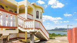 Un edificio de varios pisos con una escalera que lleva a un balcón, vista al mar y un paisaje montañoso al fondo.
