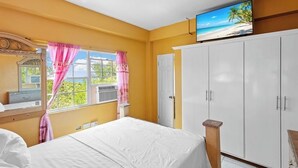 Un dormitorio con cama, armario, televisor y ventana con cortinas.