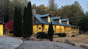 Un chalet à deux étages avec une façade en pierre, un porche couvert et un escalier menant à l’entrée.