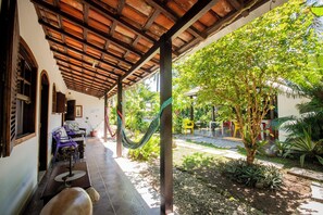 A covered outdoor area with a tiled floor, a hammock, and a small garden with plants and a tree. - Pousada Chalé Suiço (Paraty)