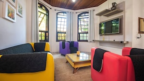 Une pièce avec un plafond en bois, de grandes fenêtres, un téléviseur à écran plat et des meubles aux couleurs vives.