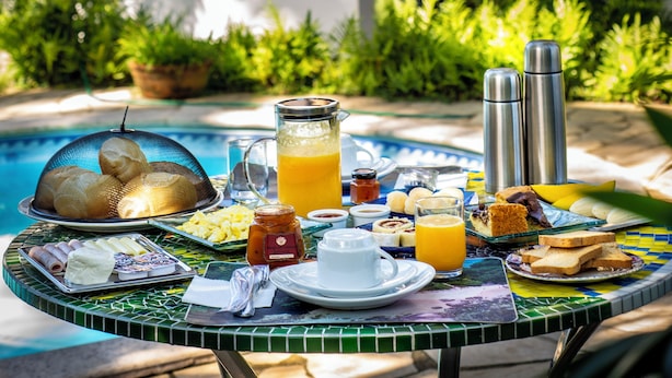 Un buffet de petit-déjeuner avec divers aliments et boissons, installé sur une table au bord d’une piscine.