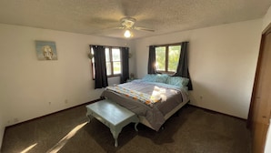 Une chambre à coucher avec un lit, une table de chevet, un ventilateur de plafond et une fenêtre avec des rideaux.