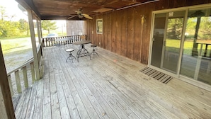 Une véranda couverte avec une terrasse en bois, une table ronde entourée de quatre chaises et une porte-fenêtre coulissante donnant sur une pelouse.