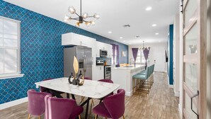 Una cocina moderna con armarios blancos, una isla de mármol y sillas moradas.
