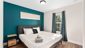 Un dormitorio con cama, mesita de noche, ventana con cortinas y lámpara en el techo.