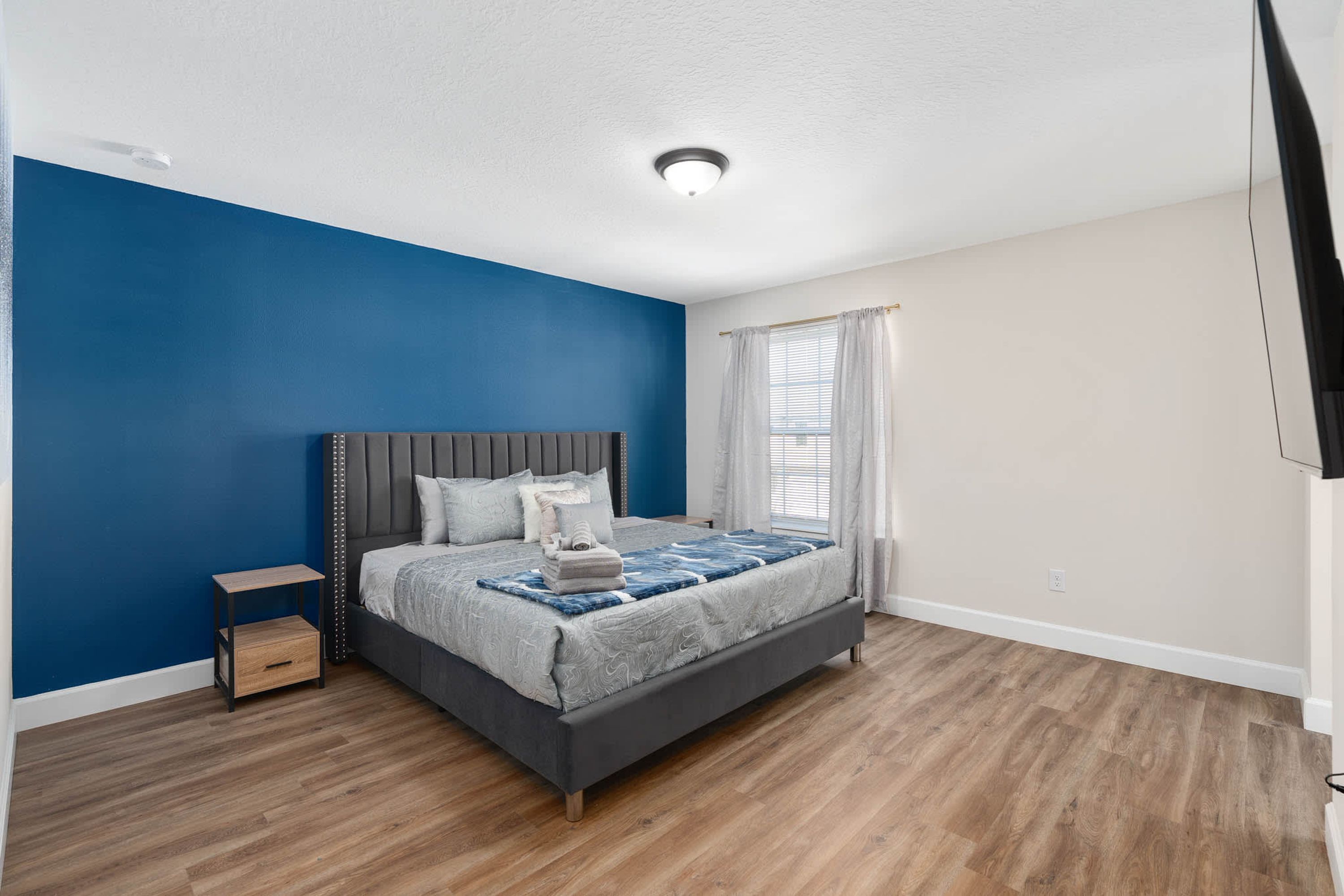 Un dormitorio con cama, mesita de noche y ventana con cortinas.