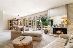 A spacious living room with a fireplace, comfortable seating, and a view of the outdoor patio. - Hello Paradise - A Private Palm Springs Retreat with Stunning Views (Palm Springs)