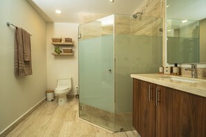 A modern bathroom with a glass-enclosed shower, a toilet, and a vanity with a mirror. - Chic Condo • King Bed • Rooftop Pool • Walk to Beach & 5th (Playa del Carmen)